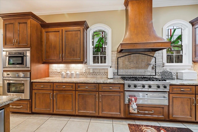 kitchen with light stone counters, light tile patterned floors, ornamental molding, custom range hood, and backsplash