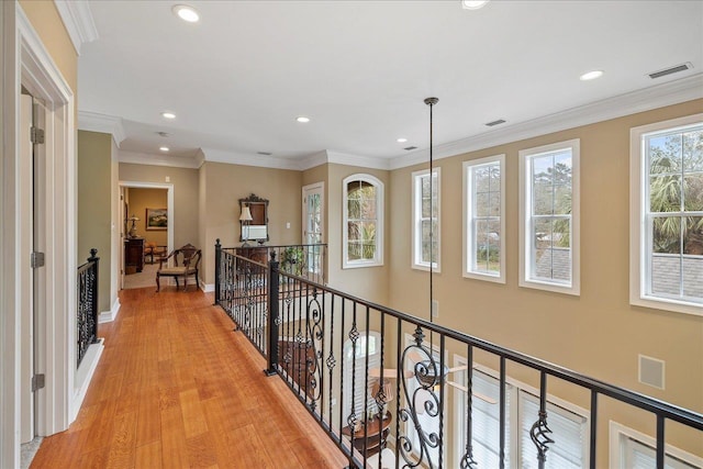 corridor featuring a healthy amount of sunlight, ornamental molding, and light hardwood / wood-style flooring