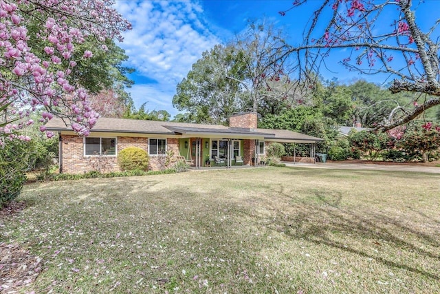 ranch-style home with an attached carport, brick siding, a chimney, and a front lawn