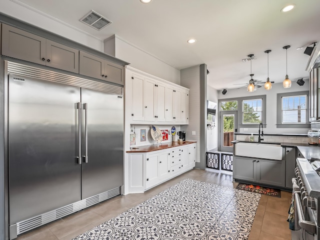 kitchen with high quality appliances, white cabinetry, sink, gray cabinetry, and hanging light fixtures