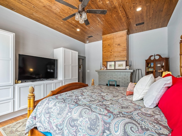 bedroom with ceiling fan, a brick fireplace, wooden ceiling, and light wood-type flooring