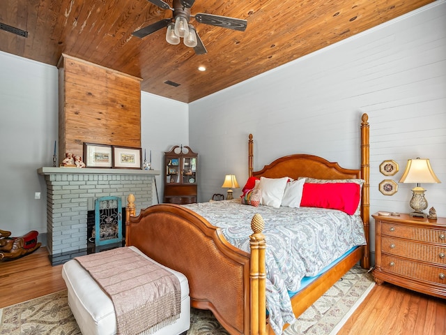 bedroom featuring ceiling fan, wood-type flooring, a fireplace, and wooden ceiling