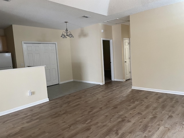 empty room featuring a chandelier, a textured ceiling, and dark wood-type flooring