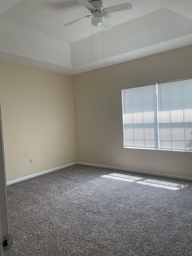 carpeted empty room featuring a raised ceiling, ceiling fan, and a textured ceiling