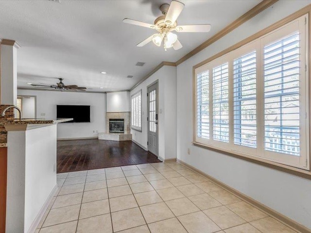 unfurnished living room featuring sink, crown molding, ceiling fan, and light tile patterned floors