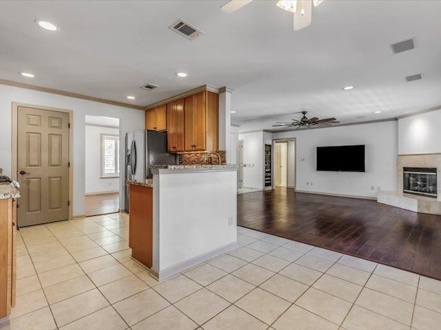 kitchen featuring ceiling fan, light tile patterned floors, light stone counters, and kitchen peninsula