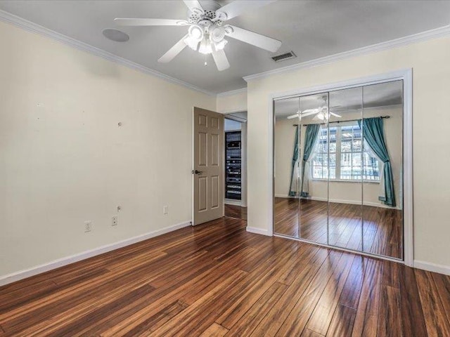 unfurnished bedroom with ceiling fan, dark wood-type flooring, crown molding, and a closet