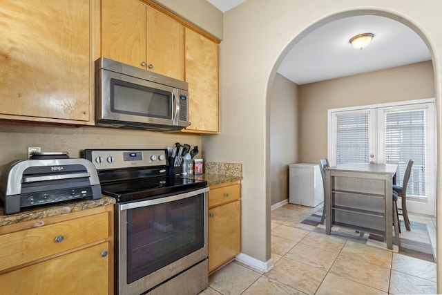 kitchen featuring dark stone counters, french doors, light tile patterned floors, and appliances with stainless steel finishes