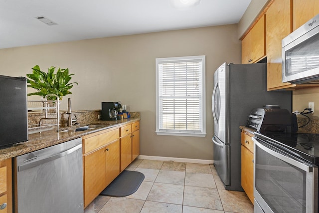 kitchen featuring stainless steel appliances, stone counters, sink, and light tile patterned flooring