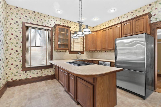 kitchen with stainless steel appliances, wallpapered walls, a peninsula, brown cabinetry, and glass insert cabinets