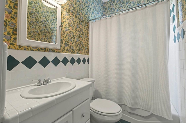 bathroom with a wainscoted wall, toilet, vanity, shower / bath combo with shower curtain, and wallpapered walls