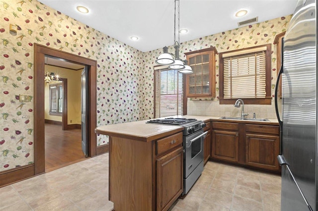 kitchen with a sink, a peninsula, visible vents, stainless steel appliances, and wallpapered walls