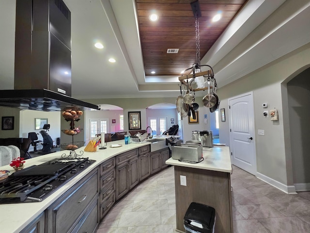 kitchen with arched walkways, black gas cooktop, a raised ceiling, open floor plan, and exhaust hood