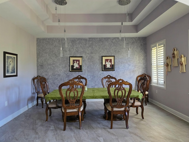 dining space with an accent wall, a raised ceiling, and baseboards