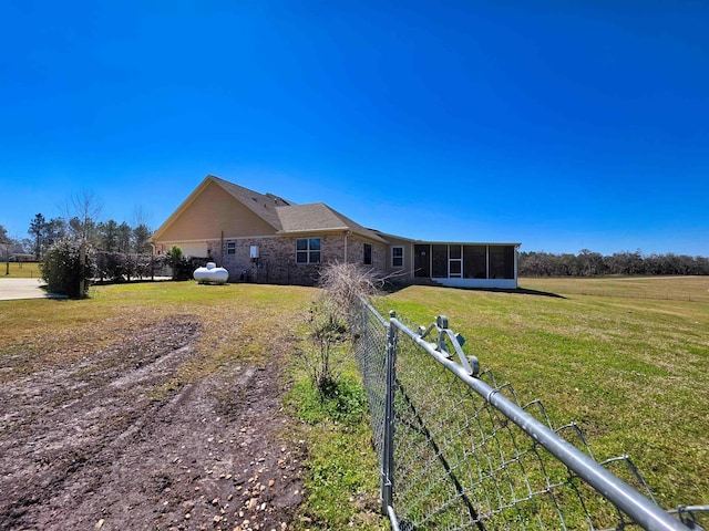 back of house featuring a sunroom, fence, a lawn, and brick siding