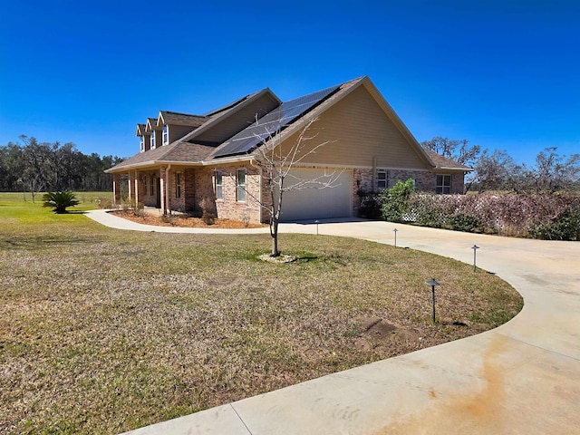 view of front of home with an attached garage, brick siding, driveway, roof mounted solar panels, and a front yard