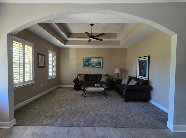 carpeted living area with baseboards, a tray ceiling, and ceiling fan