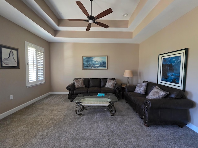 carpeted living area with a tray ceiling, a ceiling fan, and baseboards