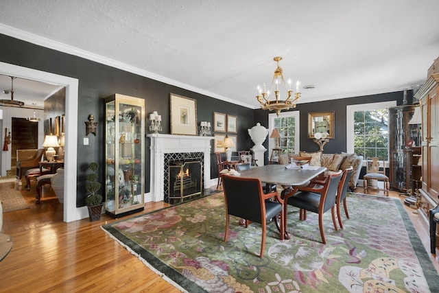 dining space with crown molding, wood-type flooring, a premium fireplace, and a chandelier