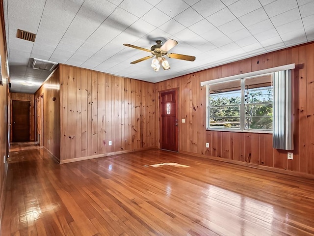 unfurnished room with ceiling fan, hardwood / wood-style floors, and wooden walls