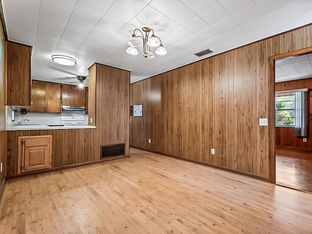 kitchen with sink, light hardwood / wood-style flooring, stove, wooden walls, and ceiling fan with notable chandelier