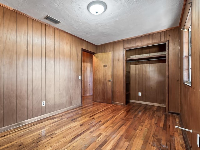 unfurnished bedroom with hardwood / wood-style floors, a closet, and wooden walls