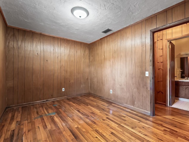 spare room featuring wood walls, hardwood / wood-style floors, and a textured ceiling