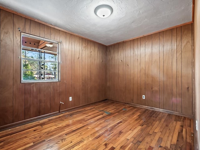 empty room with wood-type flooring, a textured ceiling, and wood walls