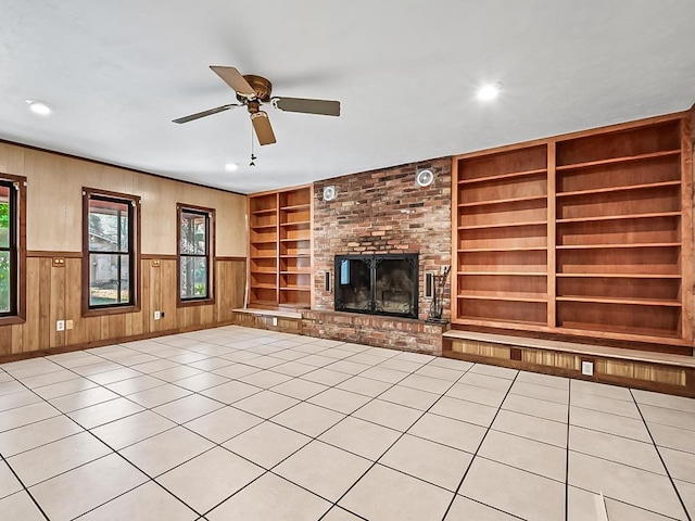 unfurnished living room with ceiling fan, light tile patterned floors, built in features, a fireplace, and wood walls