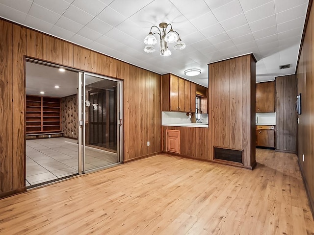 kitchen with light wood-type flooring, wooden walls, and an inviting chandelier