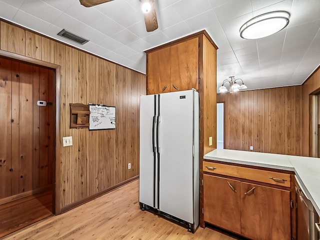 kitchen featuring wood walls, light hardwood / wood-style flooring, white fridge, and ceiling fan with notable chandelier