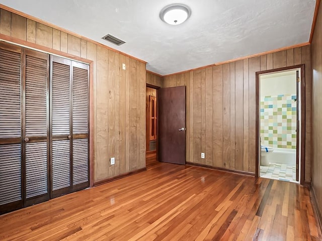 unfurnished bedroom featuring hardwood / wood-style floors, ensuite bathroom, a closet, and wooden walls