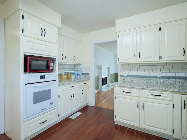 405 NW Whispering Pines Loop, Madison, FL 32340 - kitchen with white oven, decorative backsplash, dark wood-style flooring, light stone countertops, and white cabinets