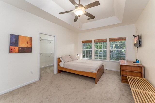 carpeted bedroom featuring a closet, a tray ceiling, a spacious closet, and ceiling fan