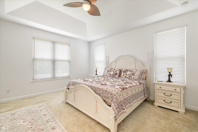 bedroom with a tray ceiling, light carpet, ceiling fan, and baseboards