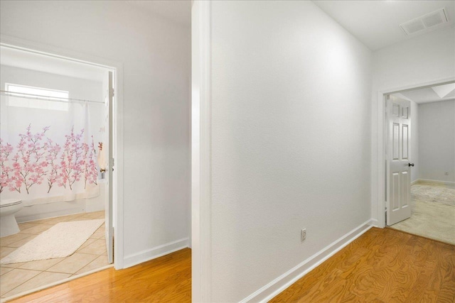 hallway with light wood-style floors, baseboards, and visible vents