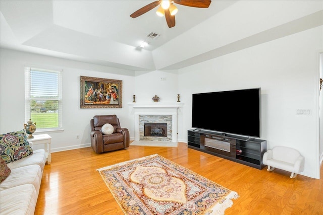 living room with a fireplace with flush hearth, light wood-style flooring, a ceiling fan, visible vents, and a raised ceiling