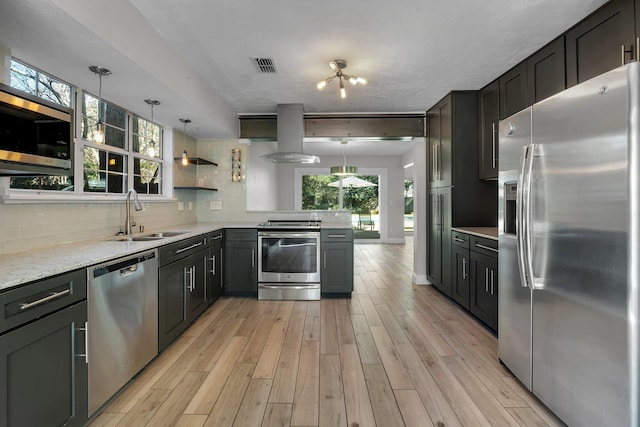 kitchen featuring appliances with stainless steel finishes, island range hood, pendant lighting, sink, and decorative backsplash