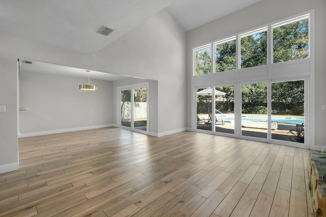 unfurnished living room with light wood-type flooring, a healthy amount of sunlight, a towering ceiling, and visible vents