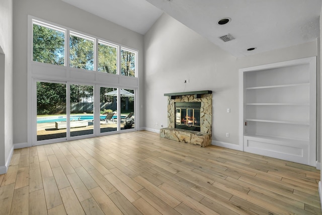 unfurnished living room with a high ceiling, light wood-type flooring, a fireplace, and built in shelves