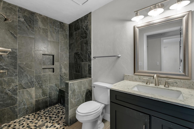 bathroom featuring a tile shower, vanity, and toilet