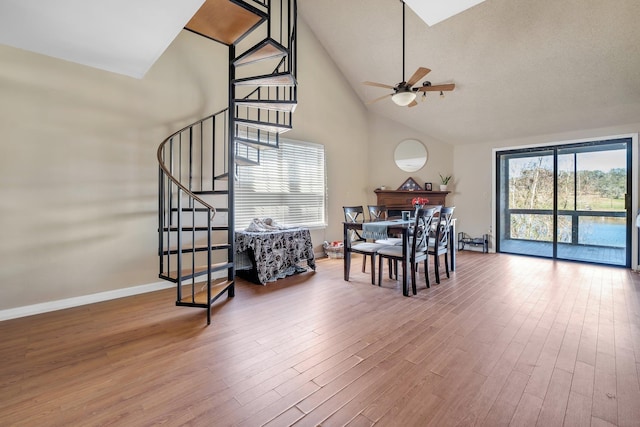 dining space featuring hardwood / wood-style flooring, ceiling fan, high vaulted ceiling, and a healthy amount of sunlight