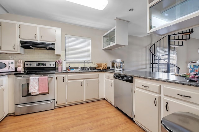 kitchen featuring appliances with stainless steel finishes, extractor fan, backsplash, light wood-type flooring, and white cabinetry