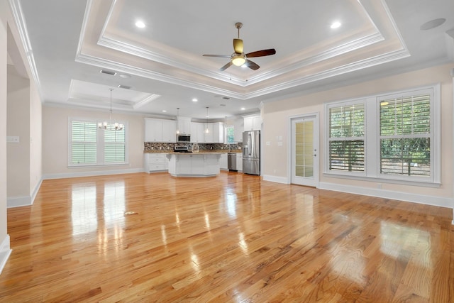 unfurnished living room featuring crown molding, ceiling fan with notable chandelier, light hardwood / wood-style floors, and a tray ceiling