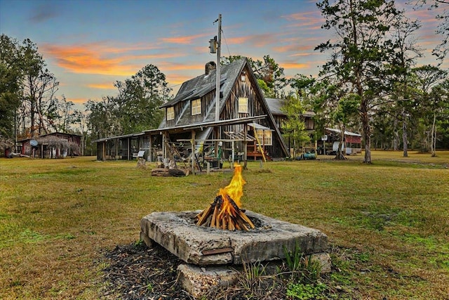 back house at dusk featuring an outdoor fire pit and a yard