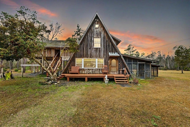 back house at dusk featuring a wooden deck, a yard, and a sunroom