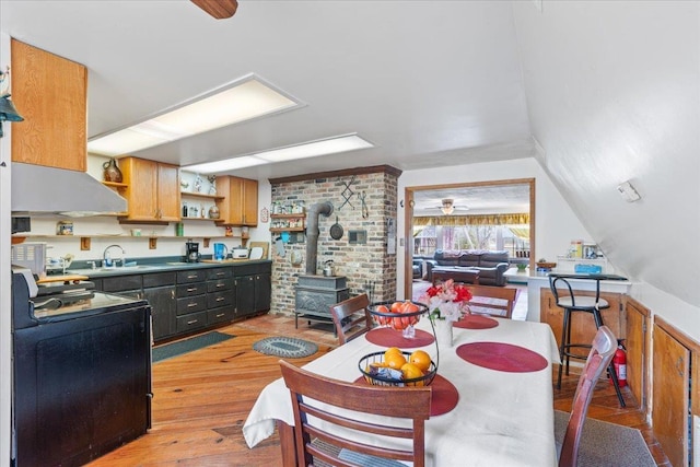 kitchen featuring sink, ceiling fan, stove, light hardwood / wood-style floors, and a wood stove