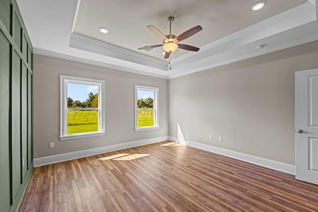 empty room featuring a tray ceiling, ceiling fan, crown molding, and hardwood / wood-style flooring