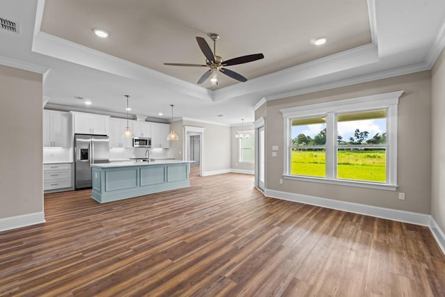 kitchen featuring appliances with stainless steel finishes, a raised ceiling, pendant lighting, a center island with sink, and white cabinets