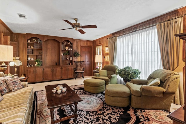 living room with built in shelves, ornamental molding, wooden walls, ceiling fan, and carpet